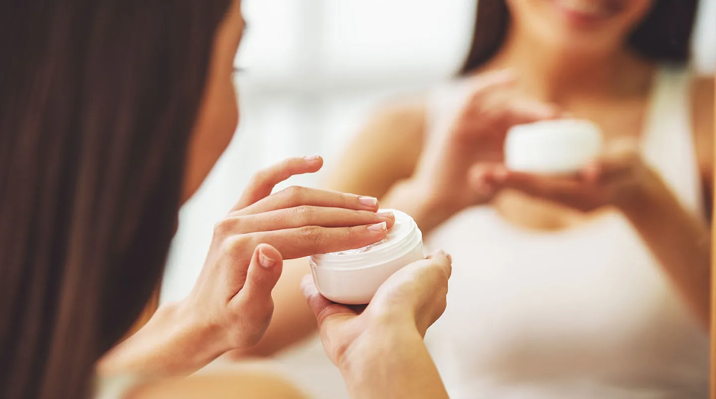 Applicering av hudvård på kvinna vid spegel