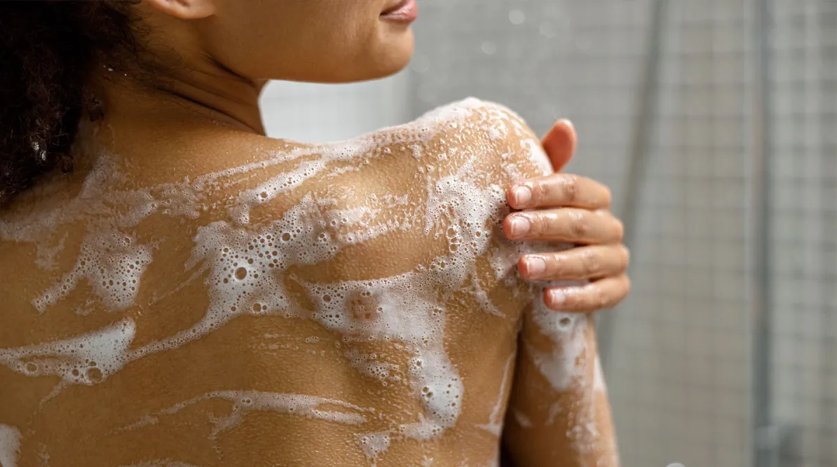 Dusch creme lödder smörjs in på ryggen i duschen av en kvinna