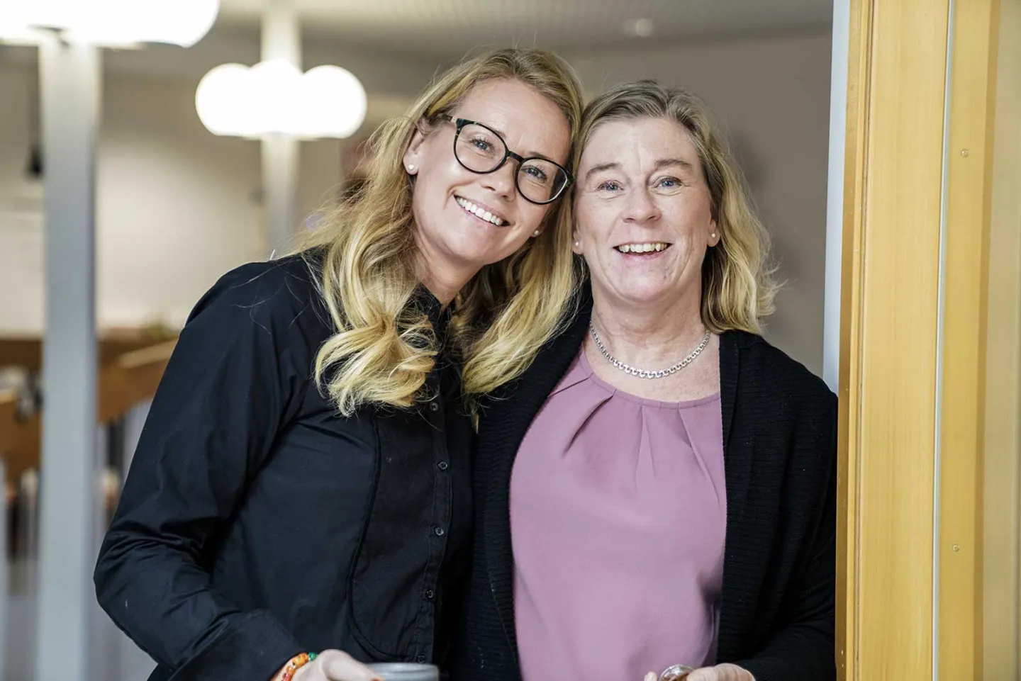 Två kvinnor som jobbar på Hardford ler och står glada bredvid varandra och håller om varandra