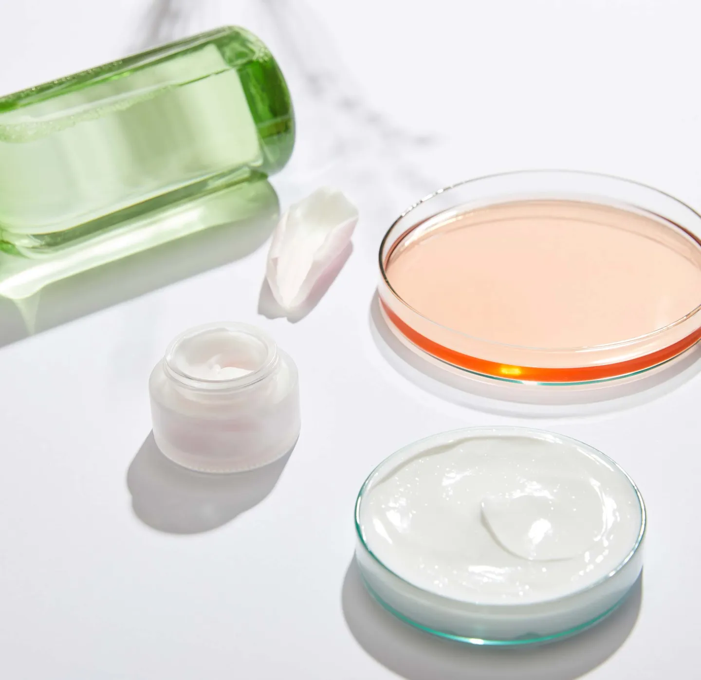 Produktutveckling krämer här i orange vätska i petriskål grön vätska i flaska och vit creme i liten burk