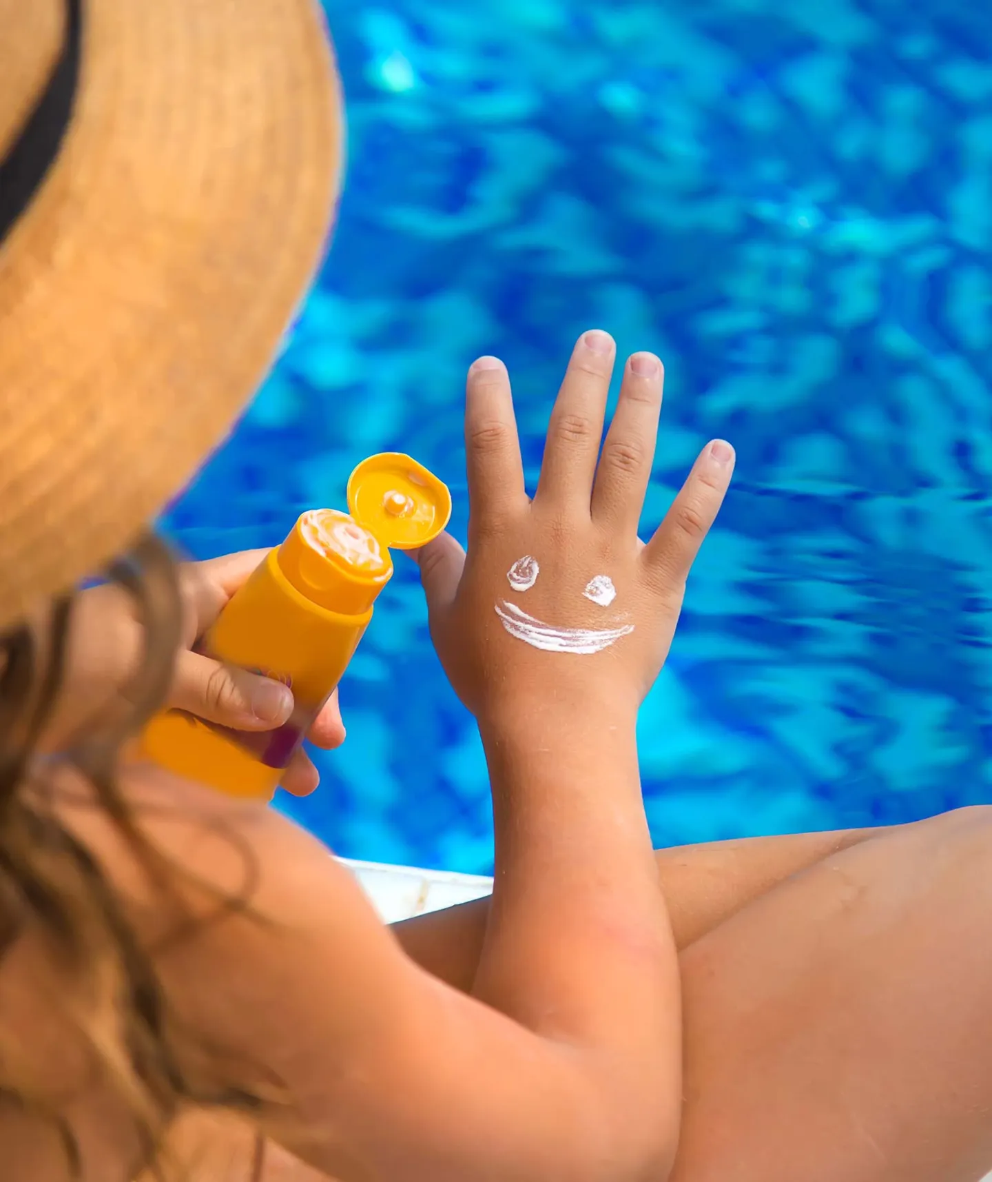 Solkräm som applicerats som en smiley glad gubbe på ett barns hand som sitter vid en pool