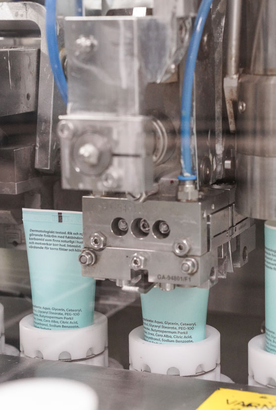 Produktion av hudvård hårvår på produktionslinje där turkosa plasttuber fylls med kosmetika